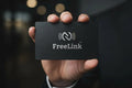 Hand holding a black NFC card with silver engraving & 'FreeLink' logo against a dark background