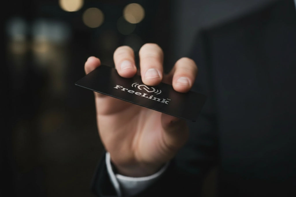Hand holding a black card with 'freelink' branding against a dark background